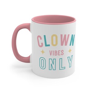 Puede incluir: Taza de cer&aacute;mica blanca con borde y asa de color rosa. La taza tiene el texto "CLOWN VIBES ONLY" impreso en letras de colores.