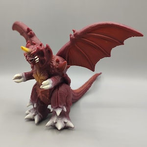 May include: A maroon-colored monster figurine with large wings, a long tail, and sharp claws. The figure has a yellow horn and white teeth. The creature is in a standing pose, with its arms outstretched.