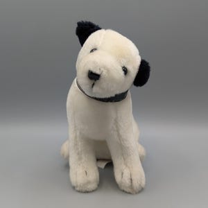 May include: A plush toy dog with a white body, black ears, and a black collar. The dog is sitting upright, with its head tilted slightly to the side. The toy has a soft, fluffy texture and is designed to resemble a friendly canine.
