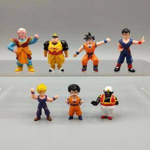 May include: A collection of seven small, colorful action figures. The figures depict various characters in dynamic poses, with vibrant colors including orange, blue, yellow, and black. The figures are arranged on a clear shelf.