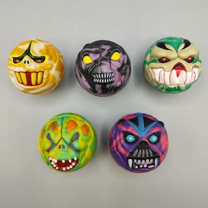 May include: Five colorful, round toys with monster faces. The toys feature various colors like yellow, green, purple, and red, with detailed facial features including teeth, eyes, and unique designs. These toys are likely collectible or novelty items.