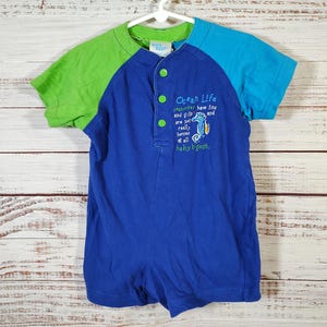May include: A blue, green, and turquoise baby romper with short sleeves. The romper has a button-up front and features the text "Ocean Life" with a seahorse graphic. The sleeves are green and turquoise.