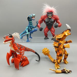 May include: A collection of colorful action figures, including a red and black raptor, a blue and green dinosaur, a red gorilla with pink hair, and an orange and yellow creature. The toys are made of plastic and have detailed features.