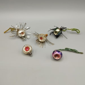 May include: A collection of vintage Christmas ornaments. The ornaments feature silver, gold, and iridescent glass bulbs with red and green accents. Some have silver tinsel-like accents and green stems.