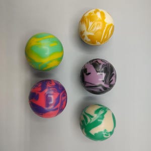 May include: Six colorful, swirled rubber balls in shades of green, yellow, purple, and red. The balls have a marbled appearance, with the colors blending together in a unique pattern. The balls are round and appear to be made of a smooth material.