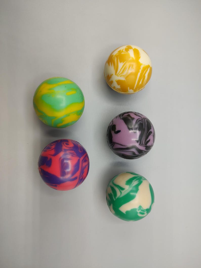 May include: Six colorful, swirled rubber balls in shades of green, yellow, purple, and red. The balls have a marbled appearance, with the colors blending together in a unique pattern. The balls are round and appear to be made of a smooth material.