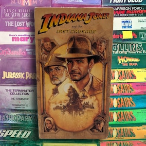May include: A vintage VHS tape of "Indiana Jones and the Last Crusade" featuring Harrison Ford. The cover art showcases Ford in a fedora, with other characters and the film's title. The tape is part of a collection of classic movies.