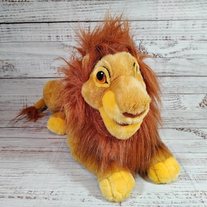 May include: A plush lion toy with a brown mane and tail, yellow paws, and a tan face. The lion has large orange eyes and is lying down. The toy is made of soft fabric and has a friendly expression.