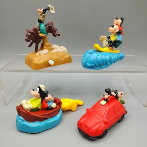 May include: Four colorful Goofy character figurines. One is riding a bull, another surfing, a third in a boat, and the last in a red car. The figurines are made of plastic and are on a clear shelf.