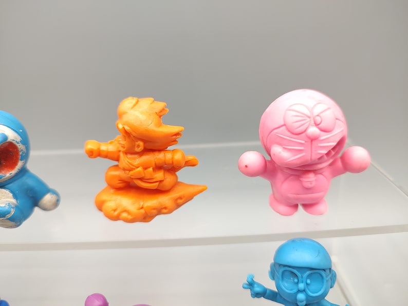 K&ouml;nnte beinhalten: Eine Sammlung farbenfroher Zeichentrickfiguren. Die Figuren umfassen eine blaue katzenartige Figur, eine orangefarbene Figur auf einer Wolke, eine rosa Figur mit einer Schleife und eine blaue Figur mit Brille. Dies sind wahrscheinlich Sammlerst&uuml;cke.