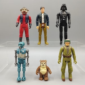 May include: A collection of vintage Star Wars action figures. The figures include characters like Darth Vader, Han Solo, and an Ewok. The figures are in various colors, including black, red, and brown. The figures are standing on a clear shelf.