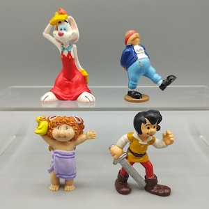 May include: Four colorful figurines are displayed. A white rabbit in a red dress and yellow hat, a man in a blue jacket and pants, a Cabbage Patch Kid with a towel, and a boy with a sword.