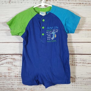 May include: Blue, green, and turquoise baby romper with short sleeves. The romper has a button-up front and features the text "Ocean Life" with a seahorse graphic. The sleeves are green and turquoise.