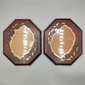 May include: A pair of octagonal wooden picture frames with a dark brown finish. Each frame features an oval center opening surrounded by intricate cut-out floral patterns and a gold-colored inner border. A small white label is visible on the left frame.