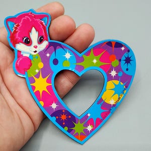 May include: A colorful heart-shaped Lisa Frank sticker featuring a pink cat with blue accents. The heart has a blue border and is filled with stars, circles, and bursts of color. The text "Lisa Frank Inc. Made in China" is visible.