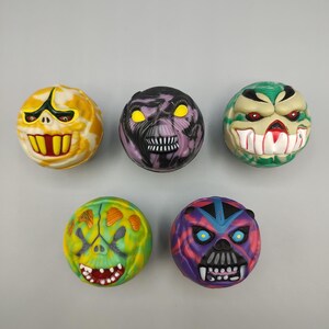 May include: Five colorful, round monster-faced toys. Each has a unique design with different colors, including yellow, purple, green, and blue. The faces feature exaggerated features like teeth and glowing eyes.