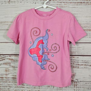 May include: Pink short-sleeved t-shirt with a purple and red butterfly design.