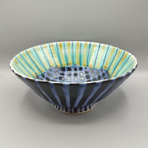May include: A large, ceramic bowl with a black and blue striped design. The bowl has a geometric pattern in the center and a light blue and yellow striped design around the rim.