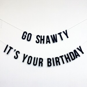 May include: Black and white banner with the text "Go Shawty It's Your Birthday" hanging on a white wall.