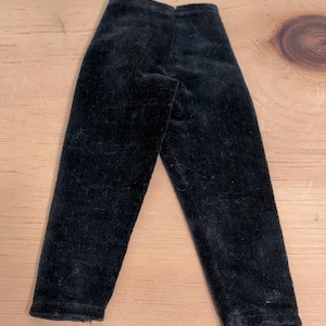 May include: A pair of black pants made from a soft, textured fabric. The pants feature a straight-leg cut with a simple waistband and hemmed cuffs. The material has a slight sheen and a fine, velvety appearance, showing a consistent solid black color throughout the garment.