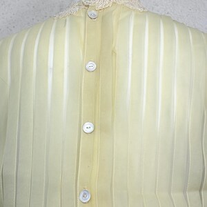 May include: A pale yellow blouse with vertical stripes and a delicate lace collar. The blouse has a button-up front with four white buttons. The fabric appears sheer and lightweight, suggesting a vintage or delicate design.