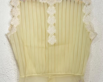 May include: Pale yellow sleeveless blouse with vertical pleats and delicate white floral lace trim. The blouse features a sheer, flowing fabric and a fitted waist. The top is hanging on a black hanger.