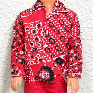 May include: A long-sleeved button-down shirt featuring a vibrant red base with a repeating black and white bandana-style floral and geometric pattern. The shirt has a classic collar, white buttons down the front, and is paired with solid red trousers.