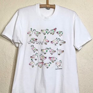 May include: White t-shirt with a colorful graphic print of ducks and the word "CALIFORNIA" at the bottom.