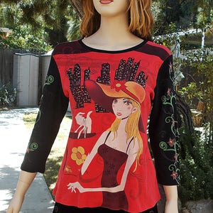 May include: A red, black, and green long-sleeved shirt with a graphic print of a woman in a hat and dress holding a shopping bag. The graphic print includes a cityscape in the background.