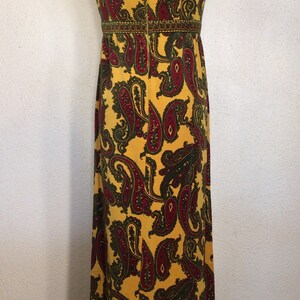May include: A long yellow maxi dress with a paisley pattern in shades of red and green. The dress has a sleeveless design and a fitted bodice.