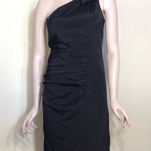 May include: A black one-shoulder dress with a ruched skirt and a single ruffle detail on the shoulder.