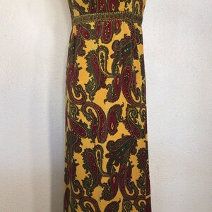 May include: A long yellow sleeveless dress with a paisley pattern in shades of red, green, and gold. The dress has a fitted bodice and a flowing skirt.