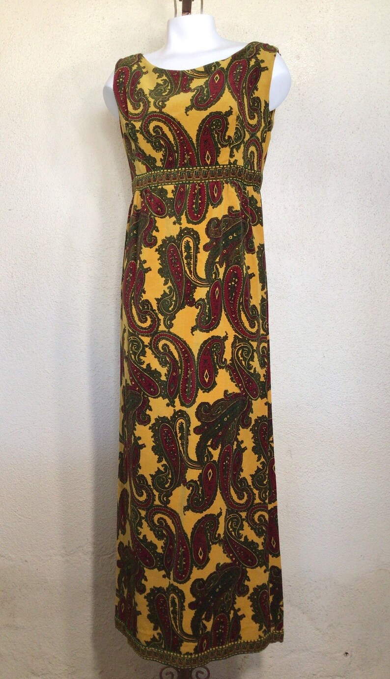May include: A long yellow sleeveless dress with a paisley pattern in shades of red, green, and gold. The dress has a fitted bodice and a flowing skirt.