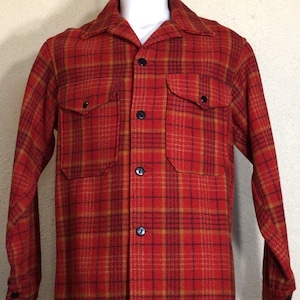 May include: A red, orange and black plaid flannel shirt with a button-up front and two flap pockets.