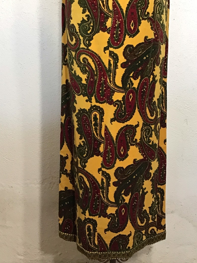May include: A long yellow skirt with a paisley pattern in shades of burgundy and green. The skirt has a gold trim around the bottom.
