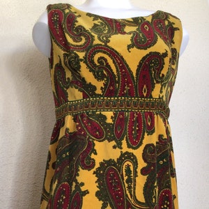 May include: A sleeveless yellow dress with a paisley pattern in shades of red and green. The dress has a fitted bodice and a flowing skirt.