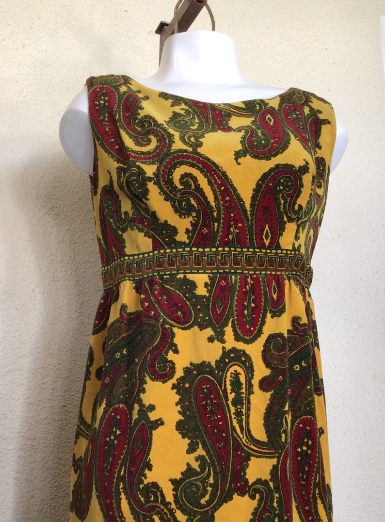 May include: A sleeveless yellow dress with a paisley pattern in shades of red and green. The dress has a fitted bodice and a flowing skirt.