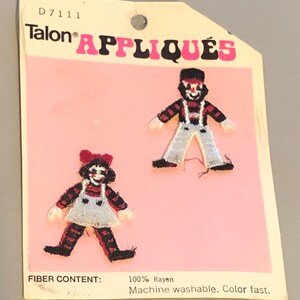 May include: A pink card with the text "Talon APPLIQUÉS" and "D7111" printed on it. Two iron-on appliqués of clowns are shown on the card. The appliqués are made of red, black, white, and blue fabric. The text "FIBER CONTENT: 100% Rayon Machine washable. Color fast." is printed on the bottom of the card.