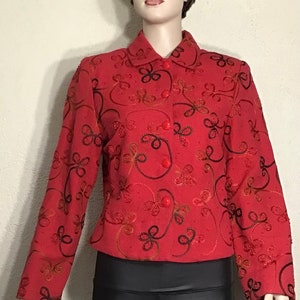 May include: A red embroidered jacket with a floral pattern. The jacket has a collar and long sleeves. The embroidery is in black and red thread.
