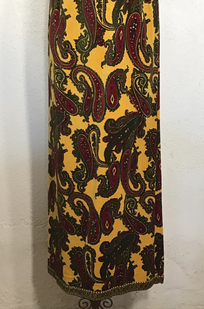 May include: A long yellow maxi skirt with a paisley pattern in shades of green and burgundy. The skirt has a gold trim around the bottom.