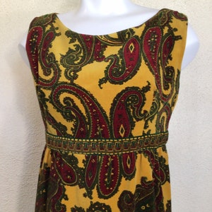 May include: A sleeveless maxi dress with a yellow background and a paisley pattern in shades of red, green, and brown. The dress has a fitted bodice and a flowing skirt.