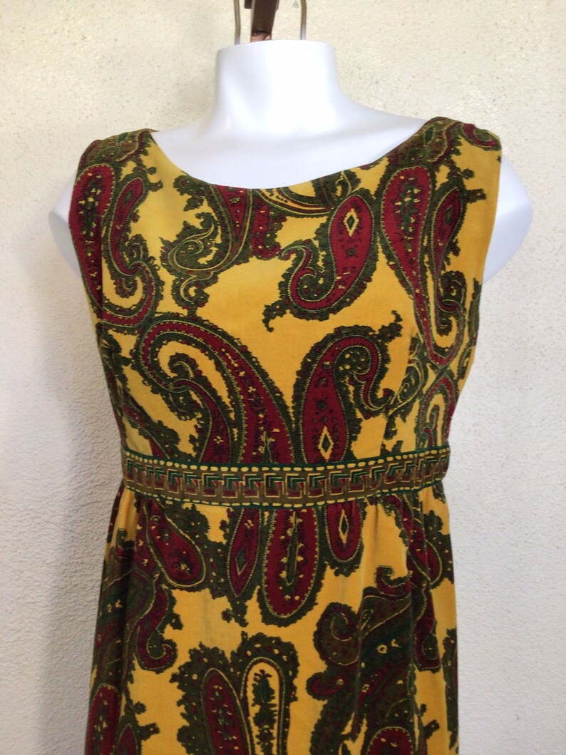 May include: A sleeveless maxi dress with a yellow background and a paisley pattern in shades of red, green, and brown. The dress has a fitted bodice and a flowing skirt.