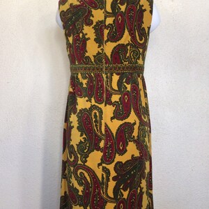 May include: A long yellow maxi dress with a paisley pattern in shades of red and green. The dress has a sleeveless design and a back zip closure.
