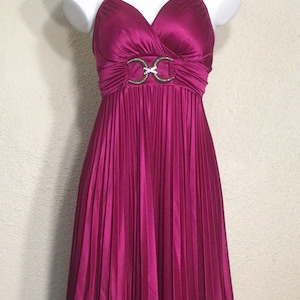 May include: A magenta pleated dress with a V-neckline and a gold-toned belt with a decorative buckle.