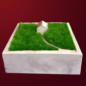 May include: A small concrete planter with a miniature white house and green artificial grass inside.