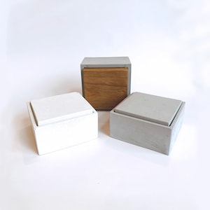 May include: Three concrete boxes with lids. The top box is gray with a wooden lid. The middle box is white with a white lid. The bottom box is gray with a gray lid.
