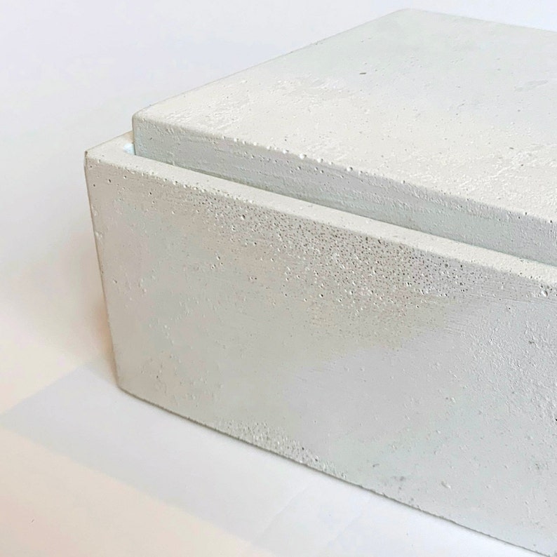 Pode incluir: Uma caixa de concreto branco com uma tampa. A caixa tem uma superf&iacute;cie &aacute;spera e texturizada.