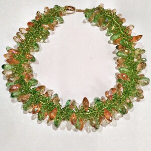 May include: A beaded necklace featuring a vibrant mix of green and orange-toned crystals. The necklace has a green beaded base with clusters of teardrop-shaped crystals. The clasp is gold-toned. This handcrafted jewelry piece is suitable for special occasions.