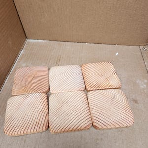 May include: Six square wooden coasters with a light brown color and a wood grain pattern. The coasters are arranged in two rows of three.