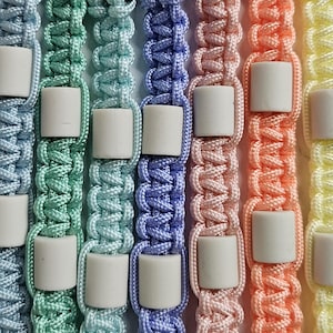 Op de afbeelding: handgemaakte halsbanden in verschillende pastel kleuren. Gemaakt van Paracord met EM keramische kralen. Natuurlijke optie tegen tegen & vlooien.